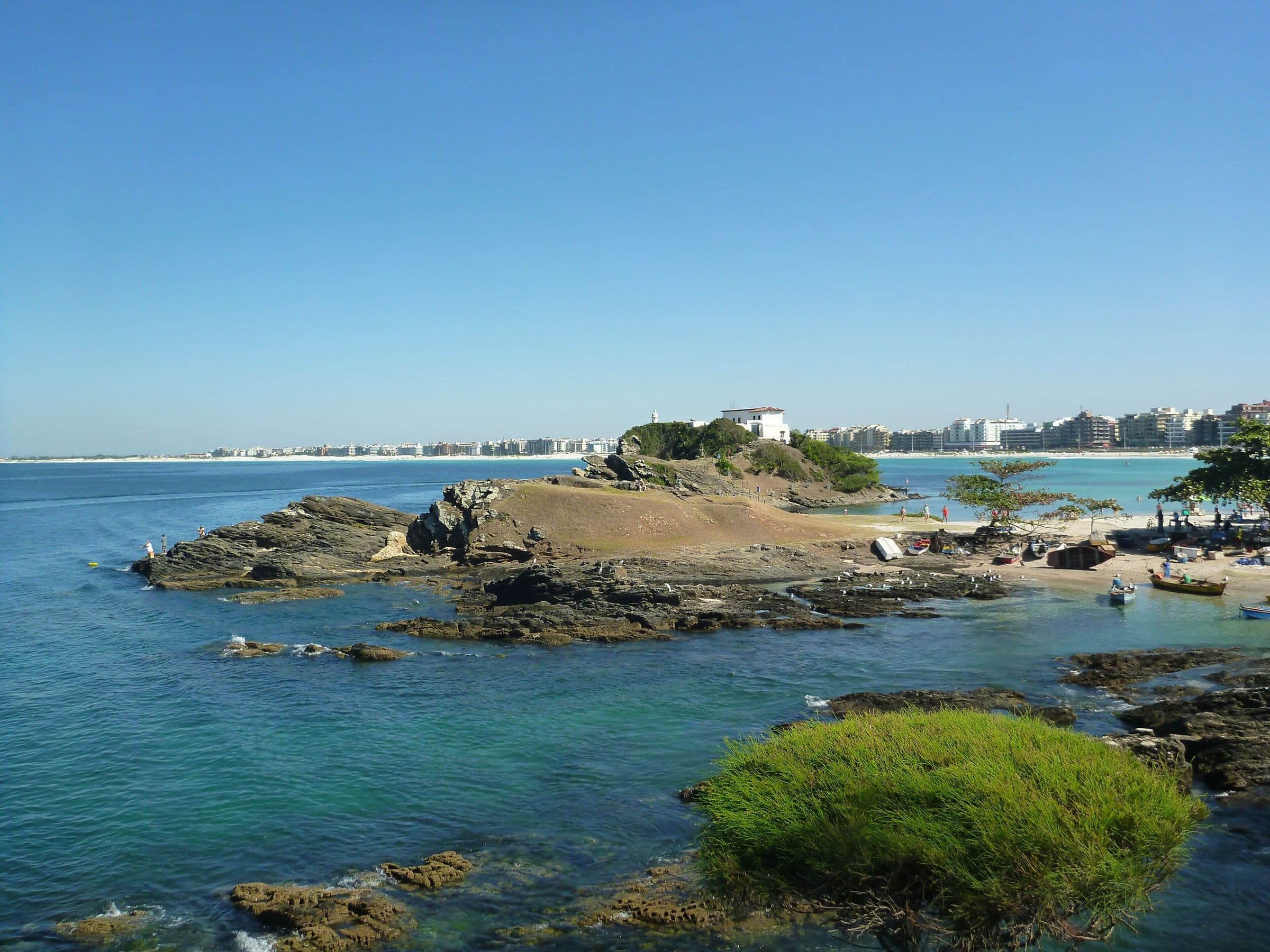 Vista aérea da foz do Canal do Itajuru junto ao Forte São Mateus, com águas turquesa, ilhotas de pedra e a orla de Cabo Frio ao fundo